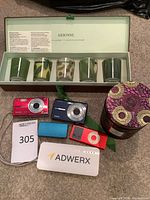Group shot of all items: Arbonne boxed candles, two Kodak cameras, iPod Nano, two power banks, Voluspa candle