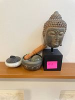 All items on shelf: Buddha head on stand, ceramic lidded jar, mortar bowl, wooden pestle with glass tip