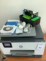 Printer with accessories atop including CD, manuals, cables and ink box