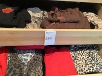 Drawer with multiple folded sweaters showing leopard prints, red, brown cable knit, grey stripe