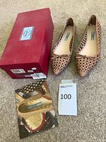 Pair of tan perforated Prada flats beside original red box and product card
