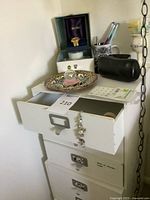 Top of white drawers showing Seiko watch in box, decorative plate, bracelet, speaker, pens