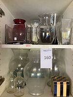 Cabinet shelves holding assortment of clear and red glass vases, small bottles, striped cube