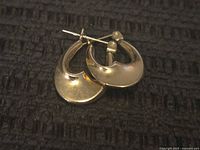 Pair of small 14k gold hoop earrings displayed on a dark textured surface.