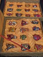 Two sets of small decorative vintage Asian masks displayed separately in yellow satin-lined boxes showing all masks in each set
