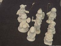 Seven white Dept 56 Snowbabies figurines on dark surface, showing full group including various winter characters with instruments and staffs.