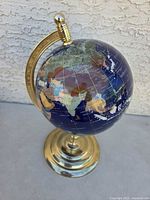 Full view of the gemstone globe mounted on a brass base, showing Asia and nearby regions.