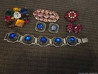 Full view of all vintage costume jewelry pieces including brooches, earrings, and bracelet on brown textured fabric