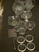 Overview of lot showing glass pitcher, creamer with handle, pedestal bowl, square dish, comb, and glass coasters with sterling rims.