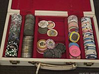 Open case revealing large assortment of variously colored vintage and fantasy casino chips organized in rows and stacks inside a white poker chip case.