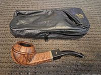 Full view of vintage Peterson's tobacco pipe next to original calfskin bag laid on fabric surface.