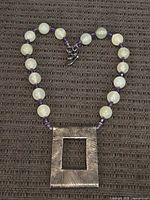 Full view of beaded necklace with rectangular sterling silver pendant resting on textured surface.