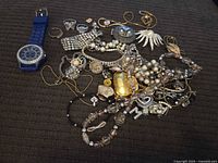 Top-down image showing a collection of assorted costume jewelry pieces and a blue watch on a dark fabric background.