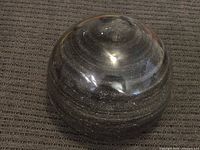 Top-down view of the black polished stone sphere showing natural striations and glossy finish.