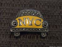 Front view of the sterling silver NYC taxi cab brooch showing yellow enamel with 'NYC' and marcasite decoration