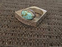 Close-up of ring front showing turquoise stone and hammered square band design.