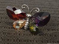 Close-up image of the butterfly-shaped ring showing colorful faceted gemstones as wings in red, purple, yellow, and amber.