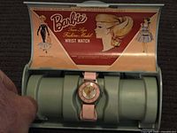 Front view of the vintage Barbie wrist watch in its original light green case with Barbie themed printed insert inside the lid.