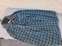 Full view of blue and green plaid wool jacket with gray shearling collar draped over a surface.