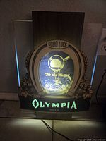 Front view of the illuminated Olympia Beer sign showing the horseshoe shape with 'Good Luck' text and glowing logo.
