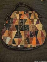 Full front view of patchwork leather purse showing various colored leather triangles sewn together with zigzag stitching and knotted handle ends