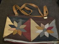 Full view of vintage patchwork purse showing front side with two floral designs and attached tan leather straps.