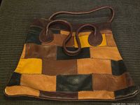 Front view of the vintage patchwork purse showing multicolored rectangular leather patches in brown, black, tan and mustard yellow with dark leather handles and trim