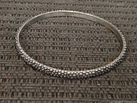 Full view of the sterling silver bracelet on fabric background showing its circular shape and dotted texture.
