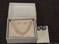 Original jewelry box open displaying freshwater pearl necklace and pair of matching freshwater pearl stud earrings, with second pair of grayish-blue pearl stud earrings on side.