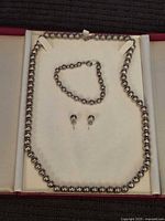 Necklace, bracelet, and earrings laid out in jewelry box, showing size and design of silver beads.