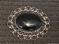 Front view shows large oval black onyx stone surrounded by ornate sterling silver filigree.
