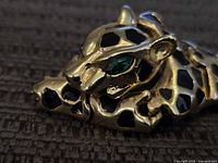 Close-up photo showing detailed view of jaguar brooch head with green gemstone eyes and black enamel spots.