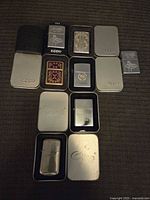 Top down view of 10 lighters in cases, 8 identified as Zippo with metal or plastic cases and 2 labeled Entice showing wear