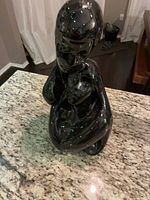 front angled view of entire black glossy abstract seated figure sculpture