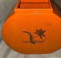 Full view showing orange glazed vase with floral motif and square opening