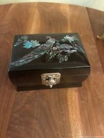 Closed jewelry box on wooden surface showing mother-of-pearl peacock design and metal clasp