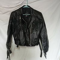 Front view of black leather fringe jacket on hanger