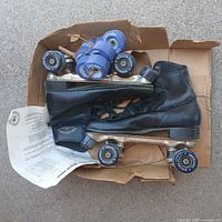 Box containing black Roller Star skates, spare blue wheels and paperwork