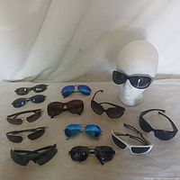 Group shot of all 13 sunglasses displayed on surface and mannequin head