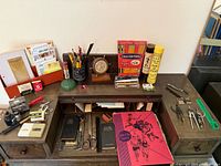 Wide view of desk contents including pencils, clock, Pick Up Sticks, letter sorter, notebooks