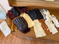 Multiple pairs of vintage gloves in various colors and materials displayed on a wooden surface.
