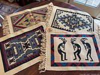 Four woven place mats with fringed edges on a wooden table, three with geometric Southwest patterns and one with Kokopelli flute player design.