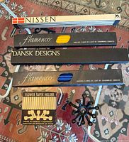 Top overview photo showing all boxes of candles and the black Dansk Designs mid century style candle holder on a patterned carpet.