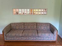 Full view of mid century sofa with Southwestern tapestry upholstery and visible wooden sides and arms.