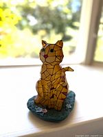 Front angled view of yellow-orange stained glass mosaic cat solar lamp with red nose and green base with flowers.