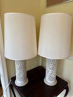 Pair of lamps on wooden table showing full view of both porcelain bodies and white fabric shades