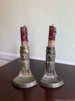 Front view of two metal candlestick holders with owl design, each holding a partially burned red and black candle.
