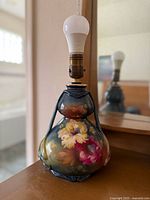 View of the lamp from front showing the floral painted pottery base and bulb on top.