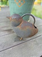 Front and side view showing the bird-shaped iron watering can with rust patina.