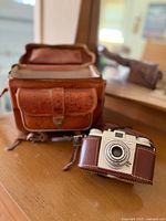 Kodak Pony 135 camera with leather carrying bag on wooden table showing overall lot items